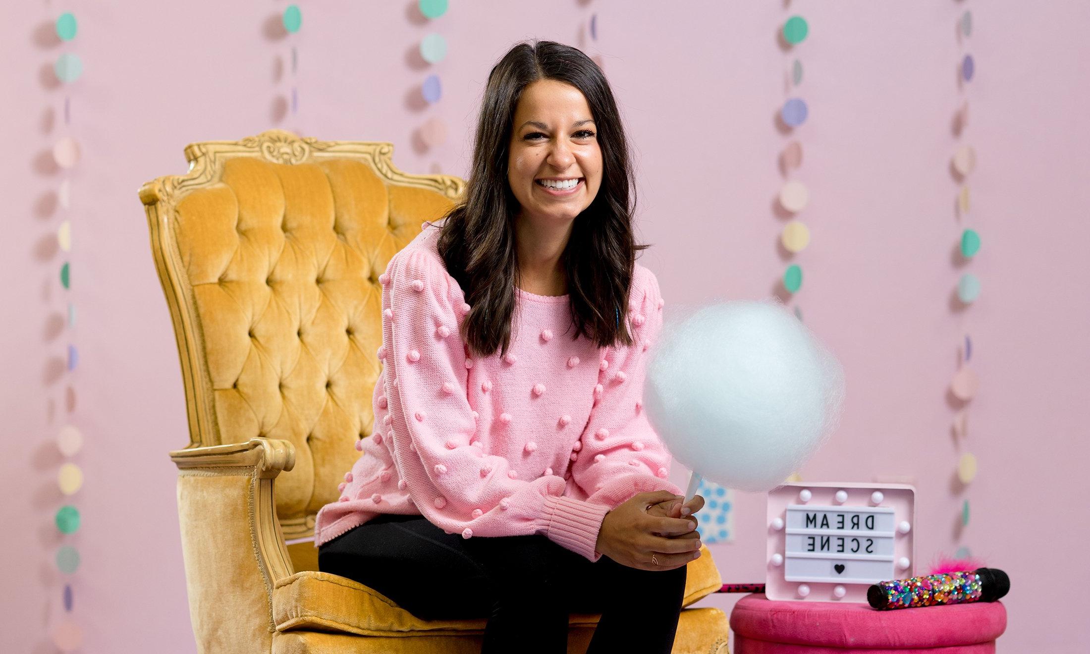 A woman in a chair holding cotton candy, to her right is a sign that reads, "Dream Scene"