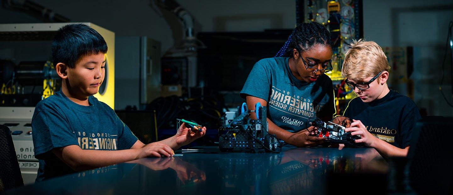 三个孩子站在实验室的桌子旁，摆弄着机械设备