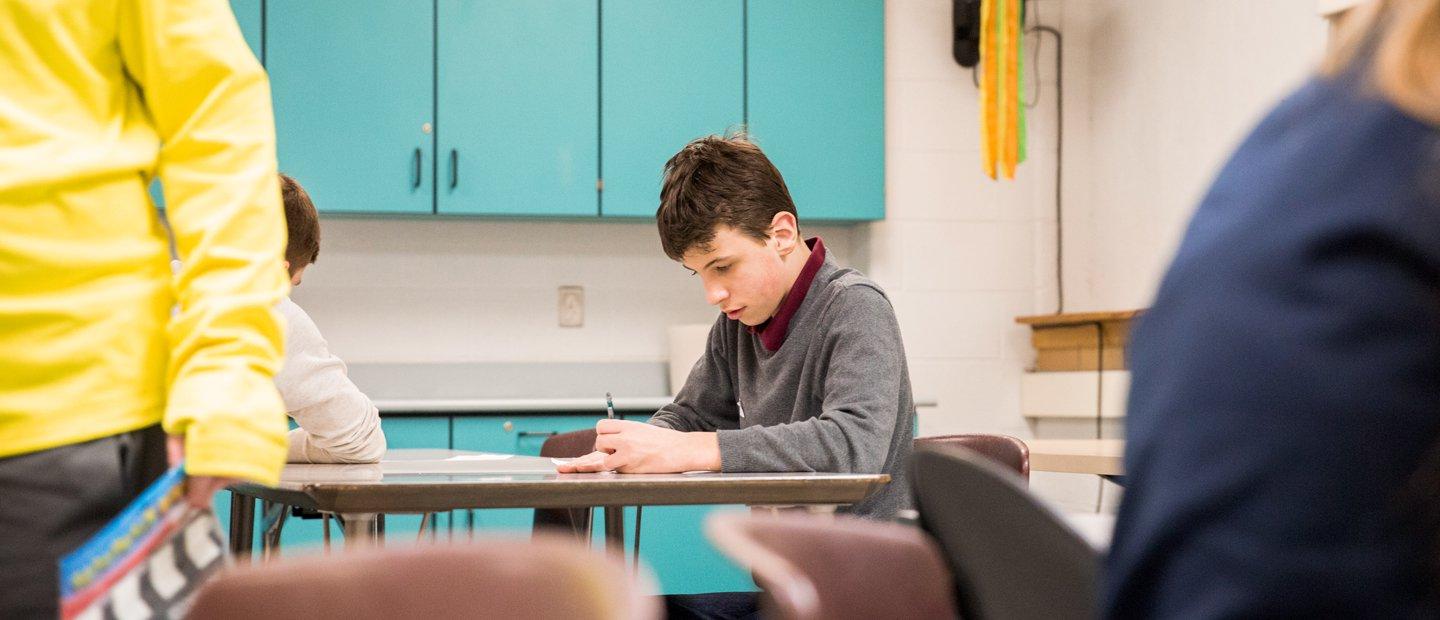 一个男孩坐在教室的桌子旁写字.
